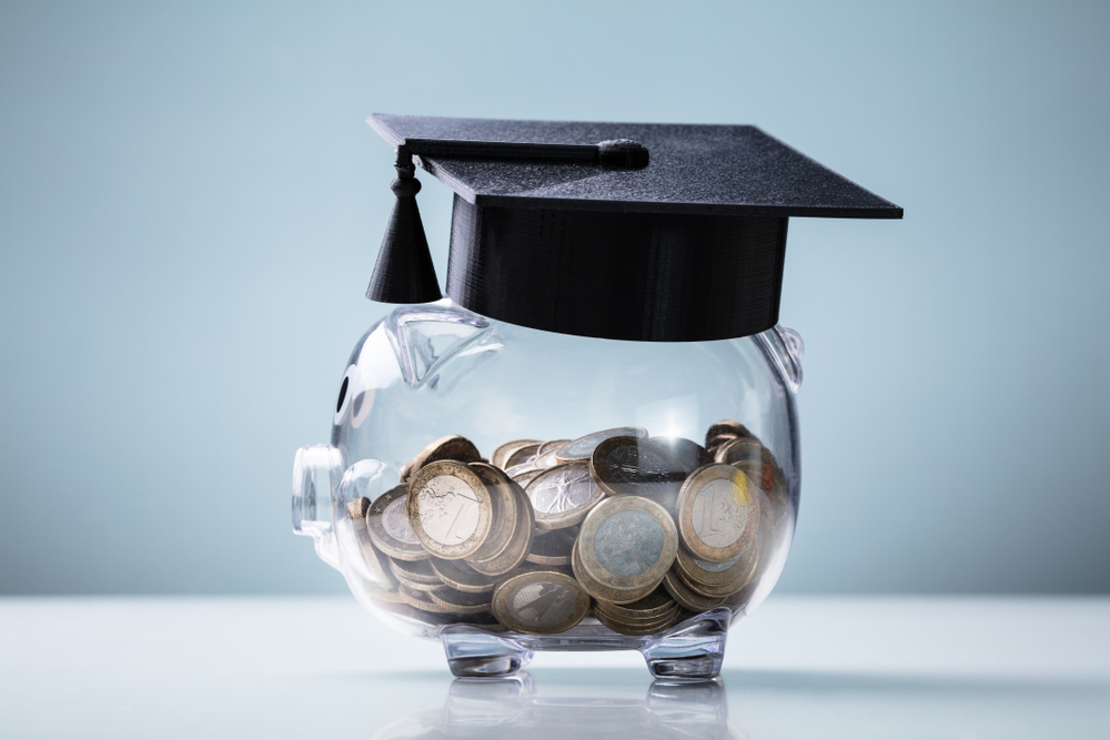 Black,Graduation,Hat,With,Transparent,Piggy,Bank,Arranged,On,White